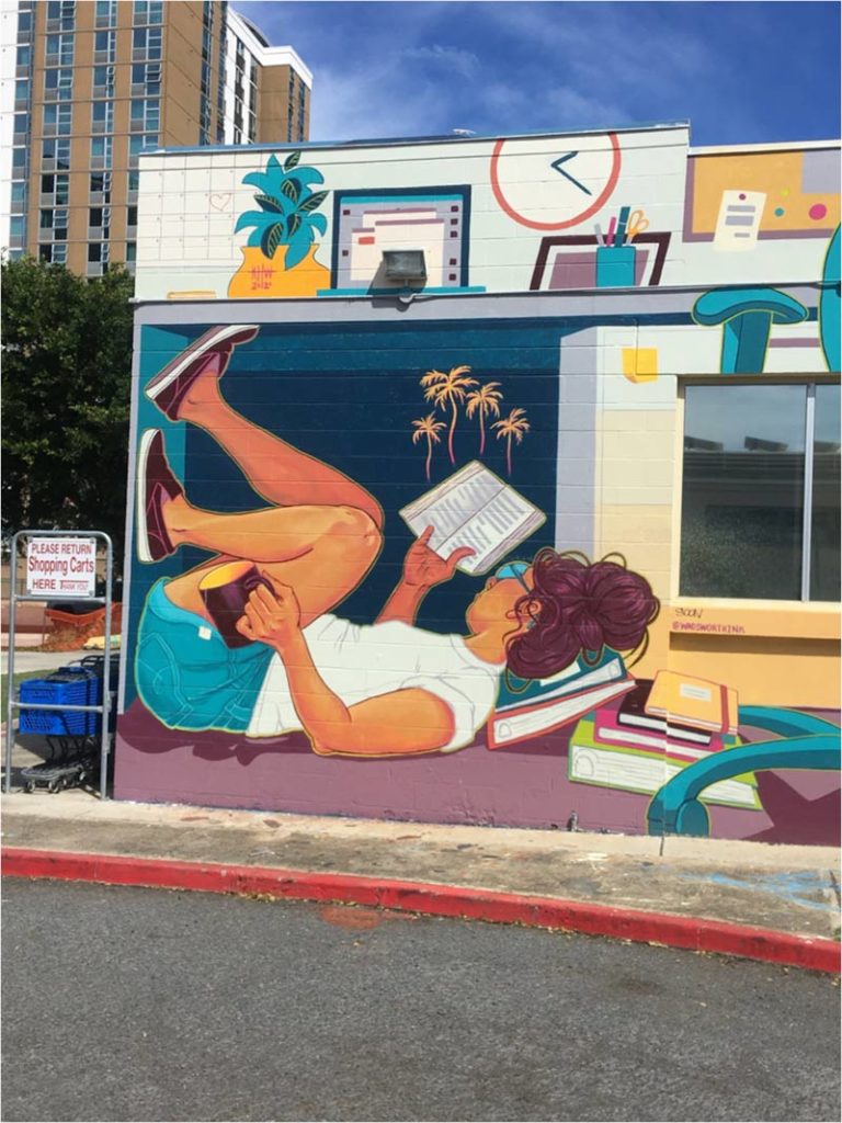 Mural of a girl lying down reading a book holding a coffee mug.